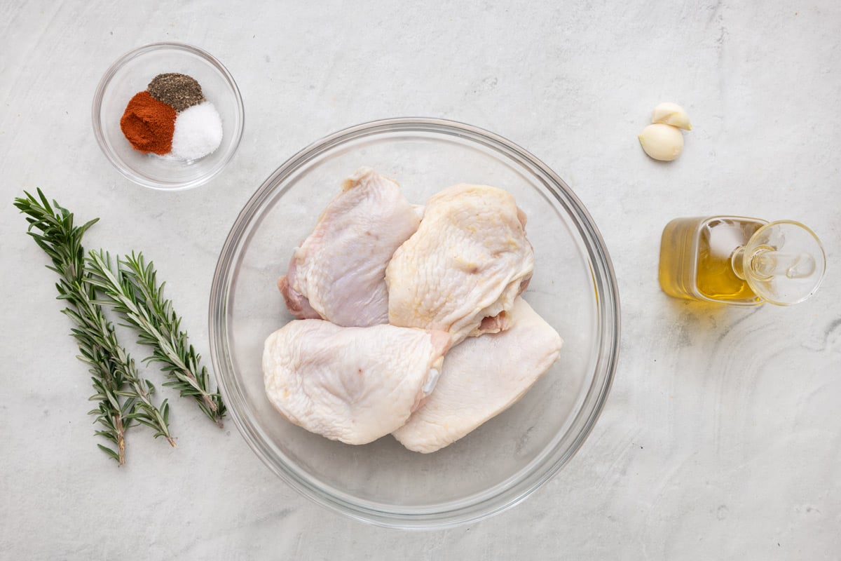 Ingredients for recipe: rosemary, spices, chicken thighs, garlic cloves, and oil.