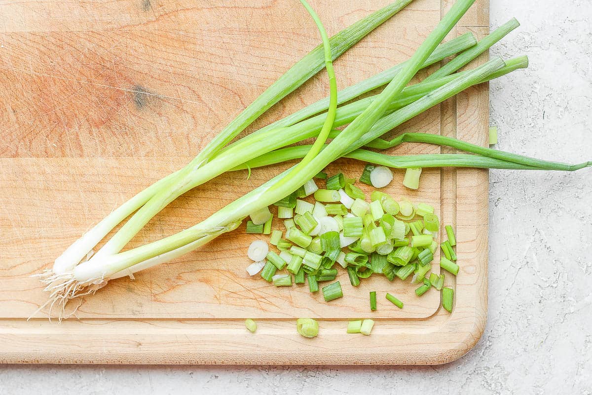 Green onions on a cutting board with some sliced into pieces.