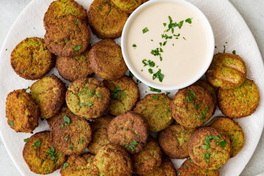 Plate full of air fried falafels with a small dish of tahini sauce and garnished with fresh herbs.