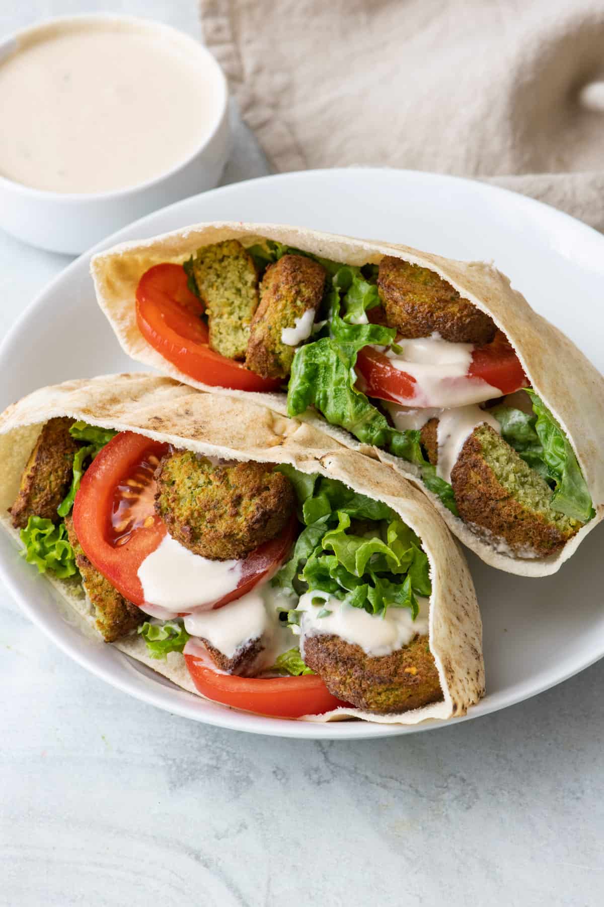 2 pita pockers with lettuce, falafels, tomato slices, and tahini sauce drizzled inside.