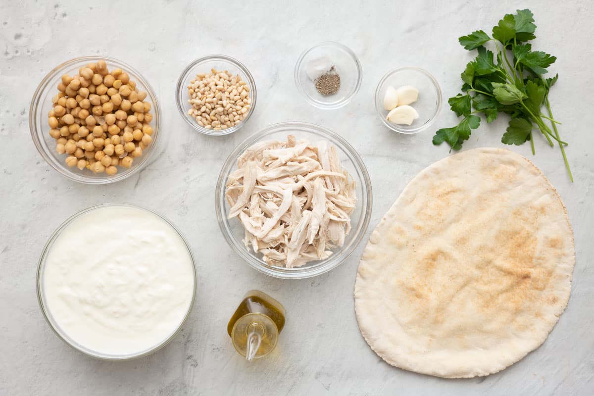 Ingredients for recipes: chickpeas, yogurts, pine nuts, shredded chicken, oil, salt and pepper, garlic cloves, fresh parsley, and Arabic-style pita.