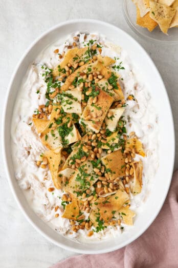 Large serving platter of chicken fatteh topped with pita, pine nuts and parsley