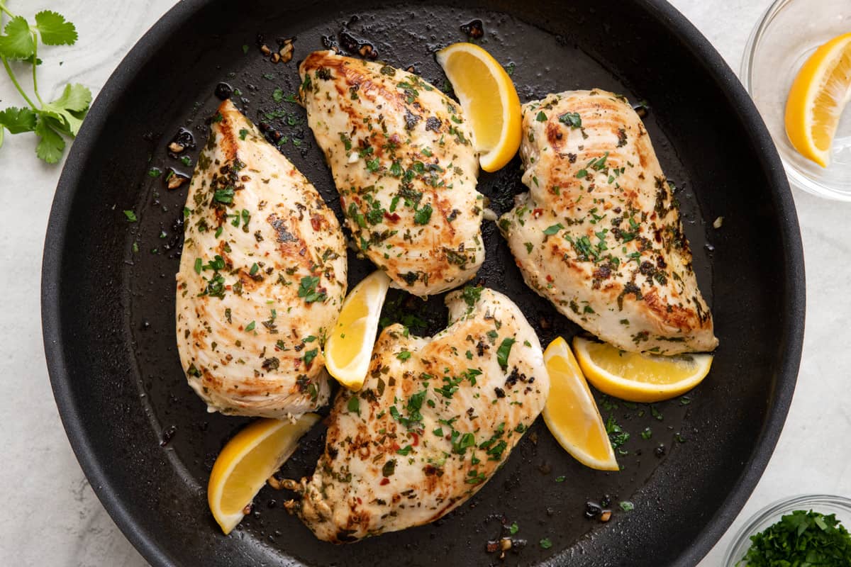 Chicken in pan garnished with extra fresh cilantro and lemon wedges.