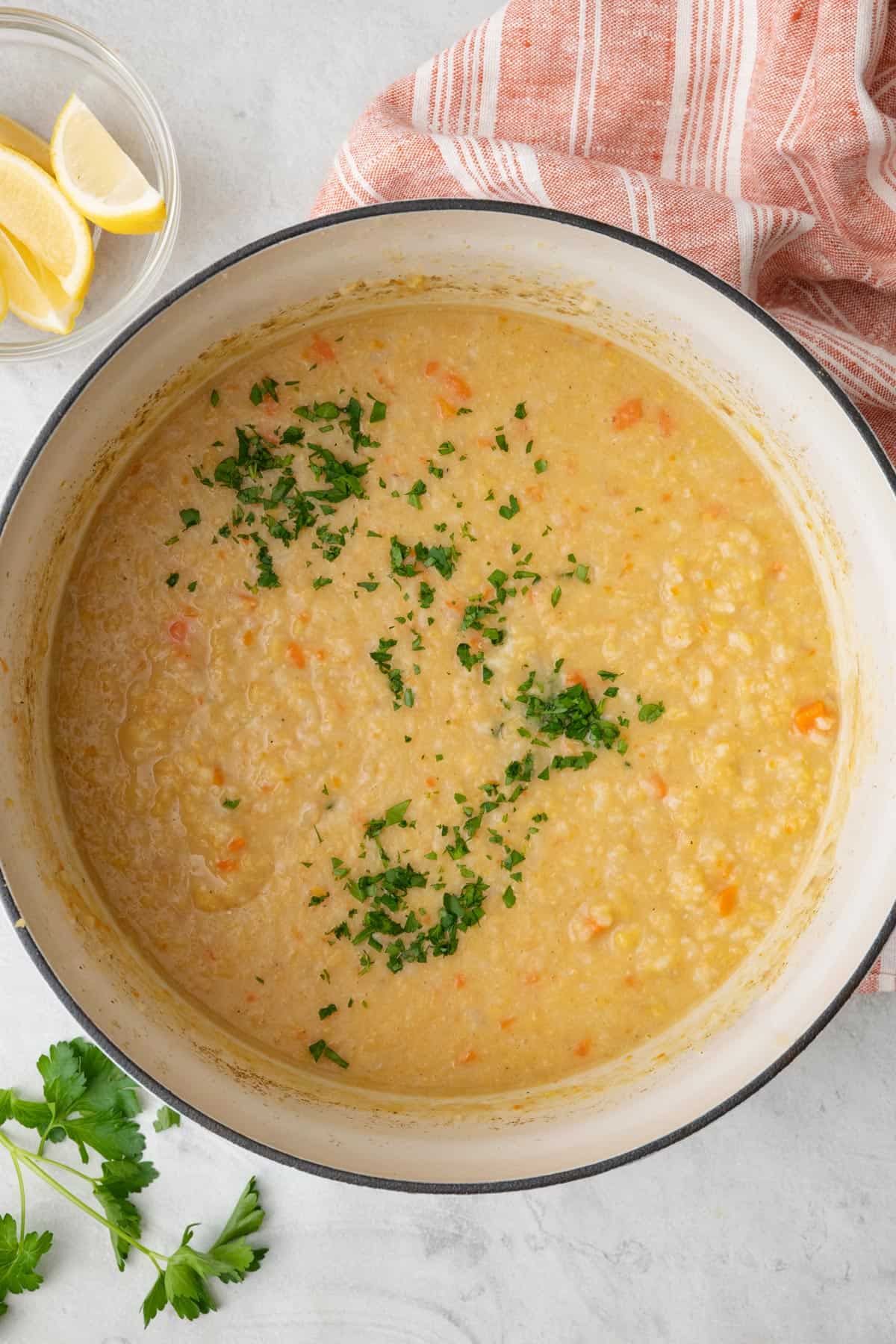 Pot of crushed lentil soup garnished with fresh parsley with lemon wedges nearby.