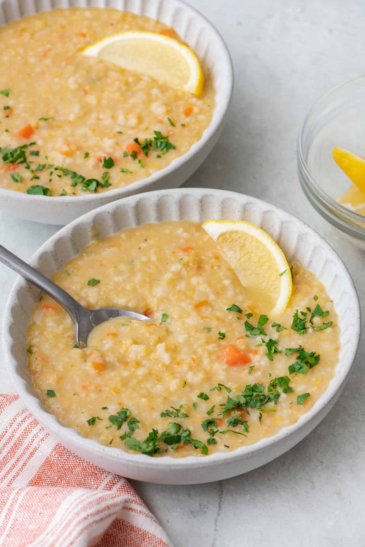 2 bowl of Crushed Lentil Soup with one close and a soup dipped in, garnished with a lemon wedge and fresh parsley.