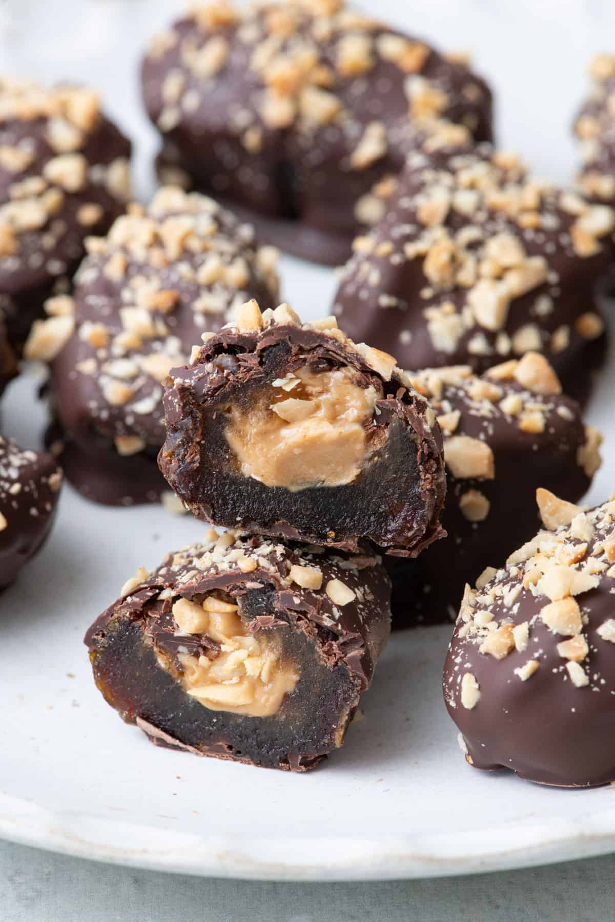 Close up of a chocolate covered stuffed peanut butter date snickers cut in half on a plate full of more date snickers.