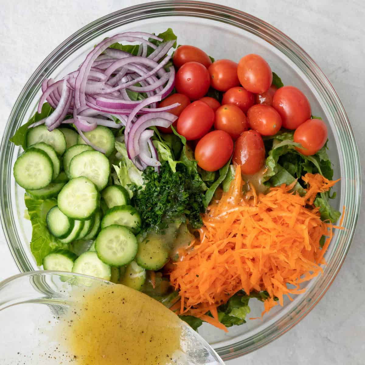 Dressing being poured over salad before tossed.