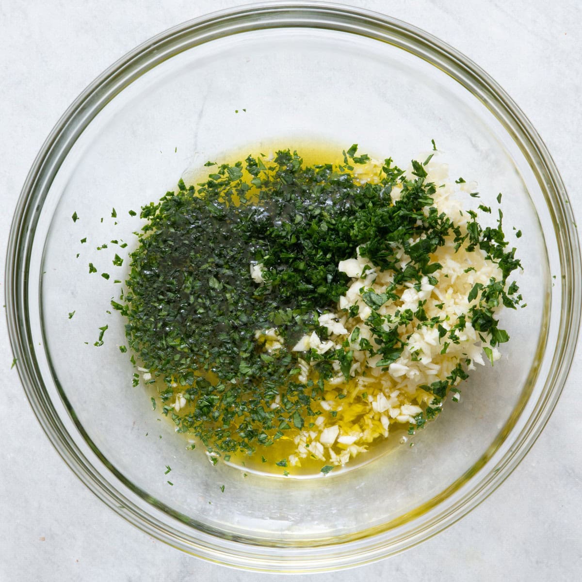 Freshly minced garlic, olive oil, parsley, chives, and salt unmixed in a bowl.