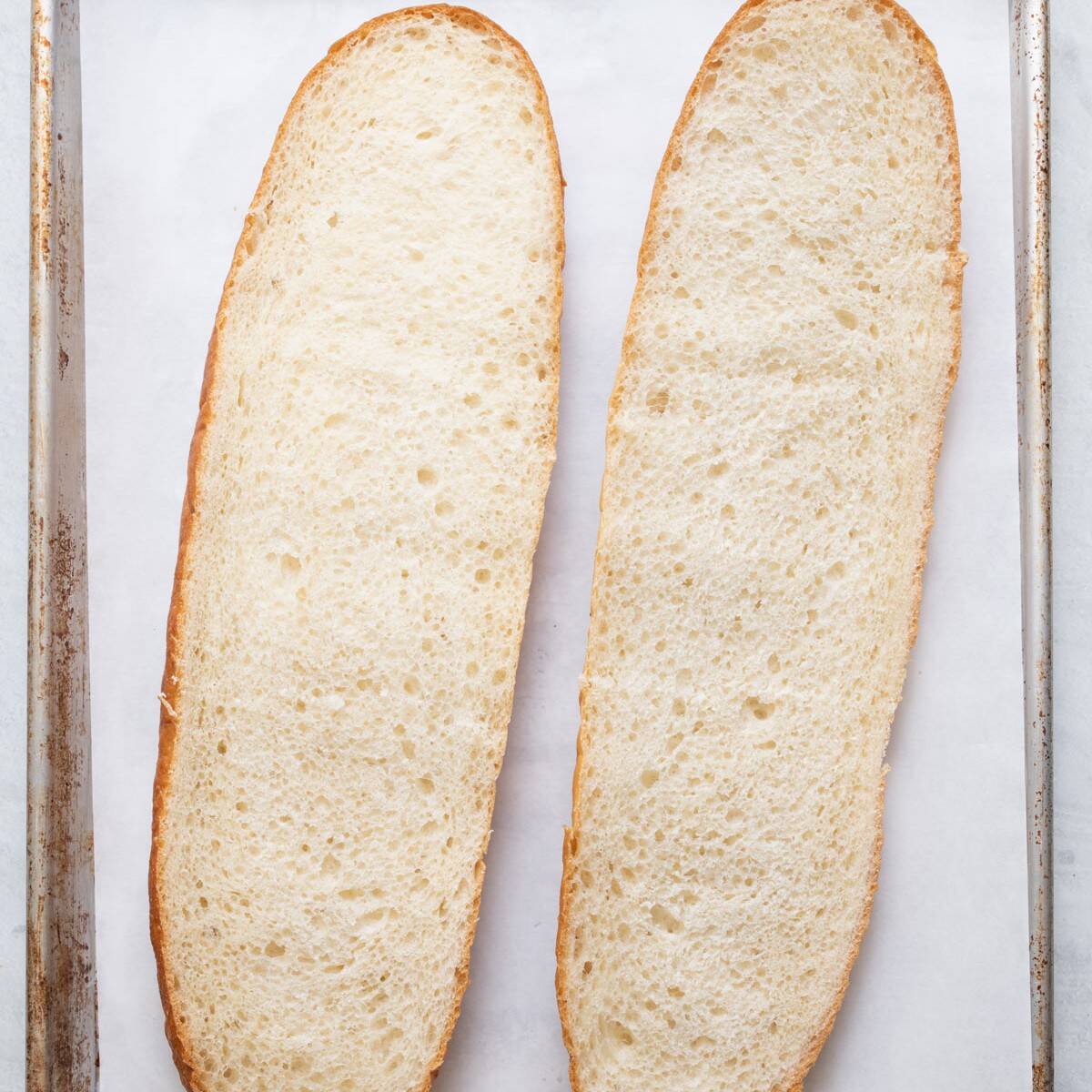 Two bread halves, cut side up, on baking sheet lined with parchment paper.