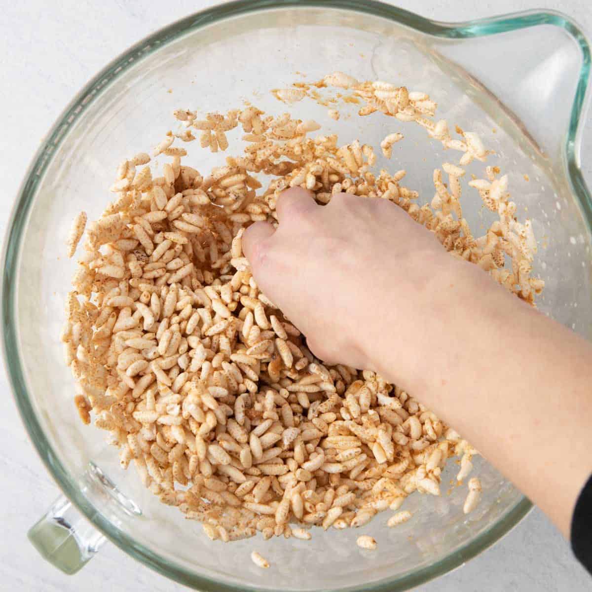Hands gently folding the rice cereal into the almond mixture.