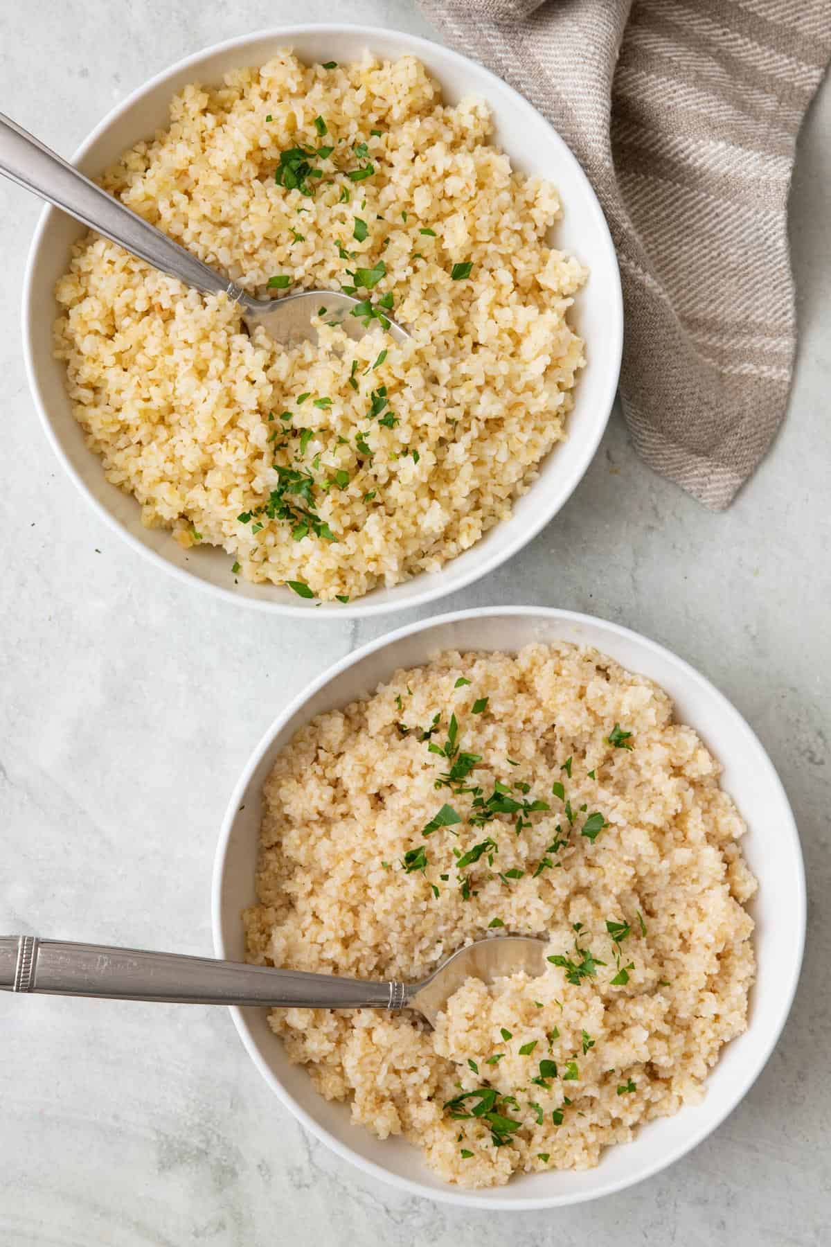 Two bowls of different sized bulgur garnished with fresh cilantro and spoons dipped into each one.