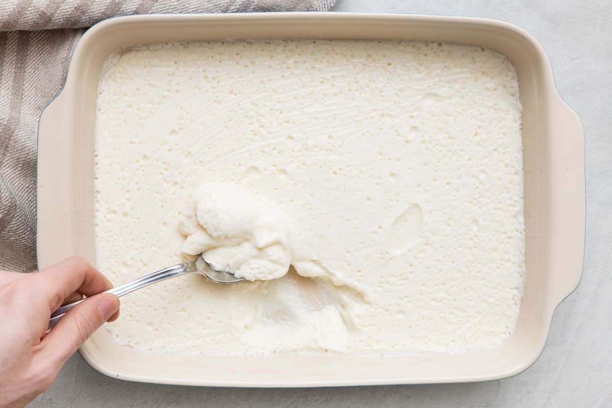 Ashta in baking dish with a spoon scooping some up to show thick yogurt-like consistency.