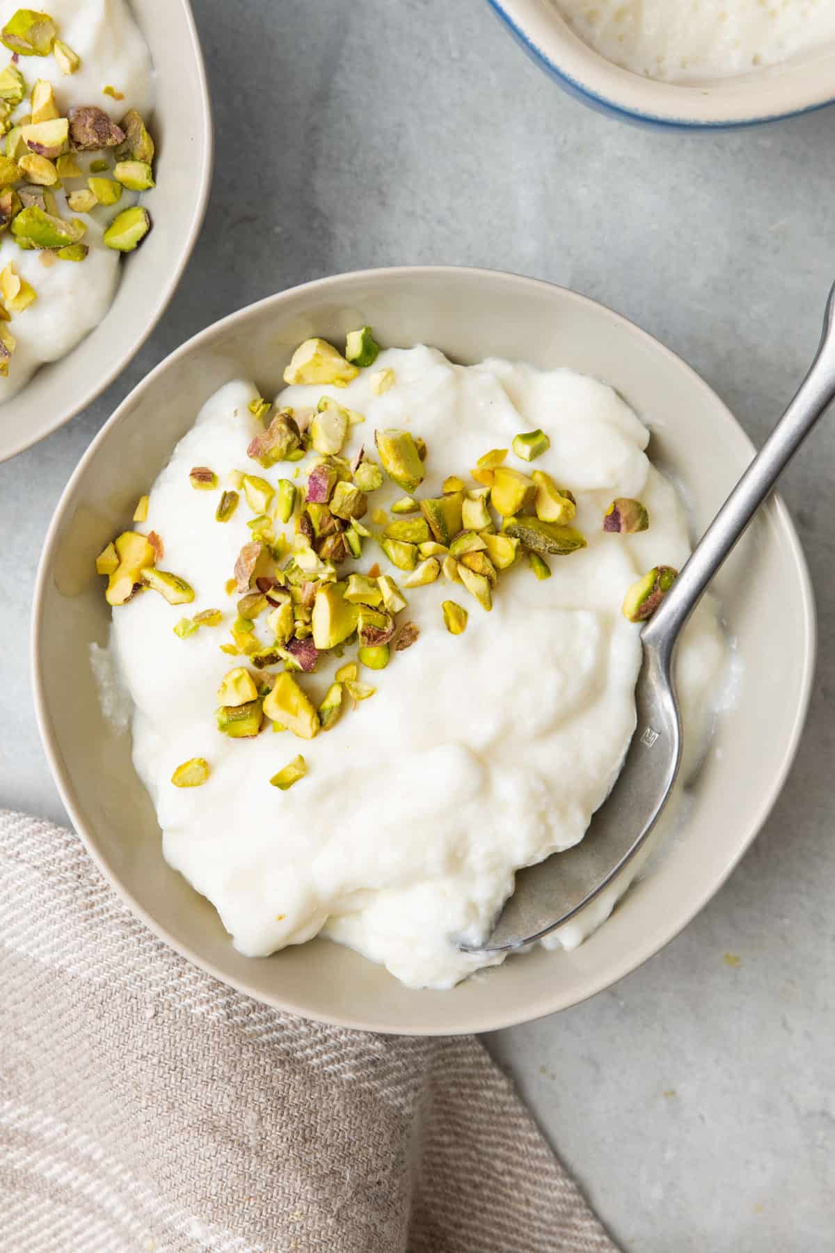 Bowl full of Ashta with crushed pistachios on top and a spoon dipped in.