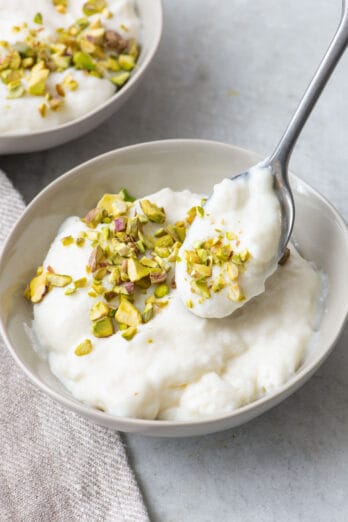 Spoon lifting up some ashta with crushed pistachios on top showing a close up of the texture.