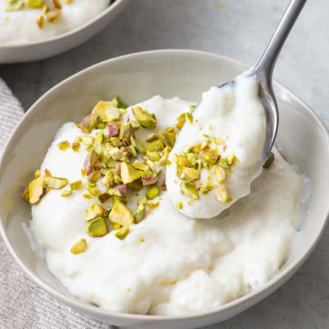 Spoon lifting up some ashta with crushed pistachios on top showing a close up of the texture.