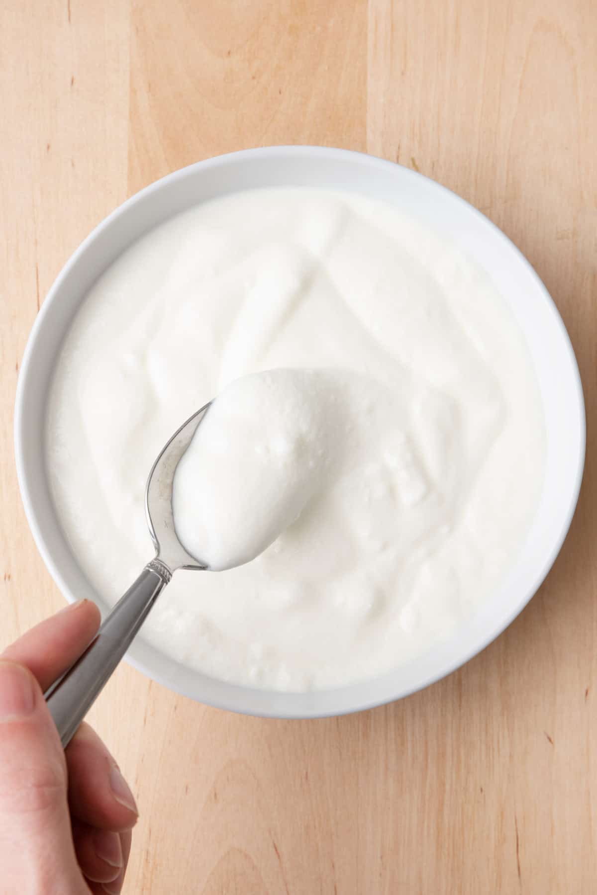 Spoon lifting up a scoop of yogurt from a white bowl on a cutting board.