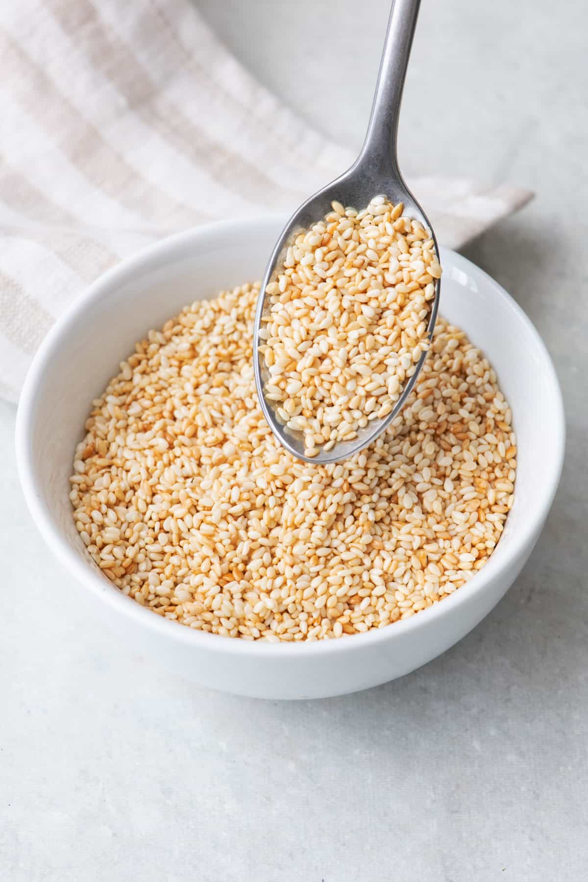 Spoon lifting up a spoonful of toasted sesame seeds from a small bowl