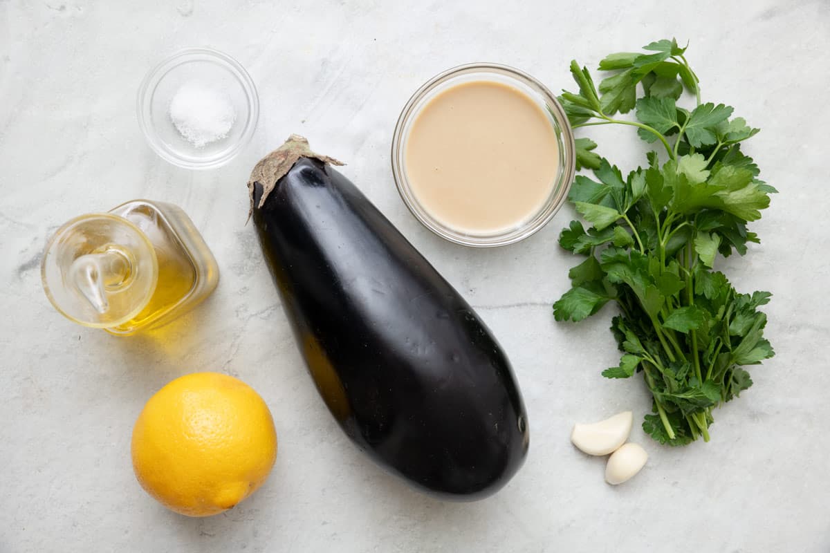 Ingredients for recipe before prepping: salt, oil, lemon, eggplant, tahini, fresh parsley, and garlic.