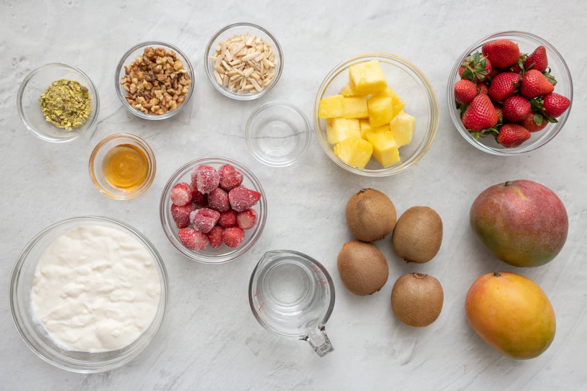 Ingredients for recipe: crushed pistachios, chopped walnuts, slivered almonds, honey, ashta, frozen strawberries, rose water, fresh pineapple chunks, whole strawberries, 4 kiwis, 2 mangoes and water.