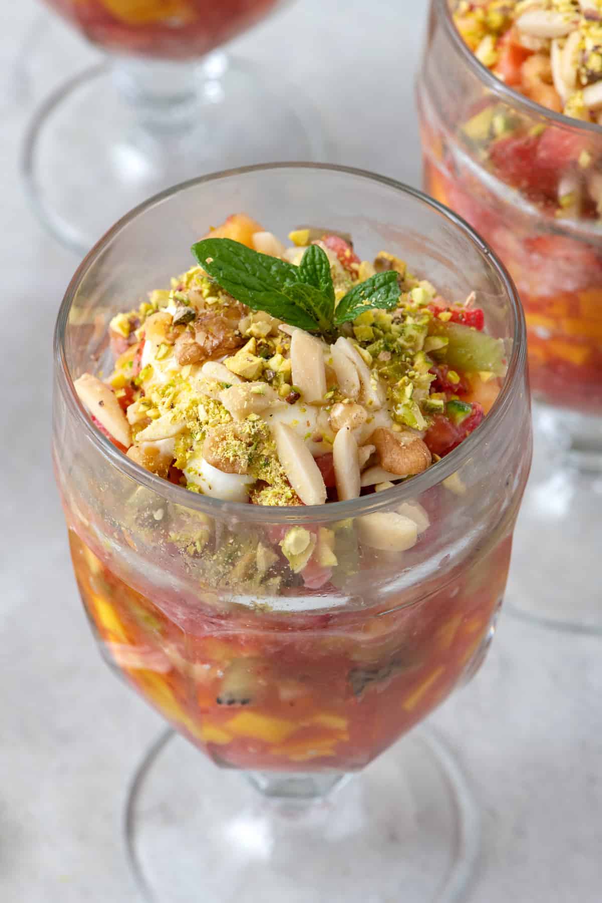 Close up of Lebanese fruit cocktail topped with ashta, chopped nuts, and mint.