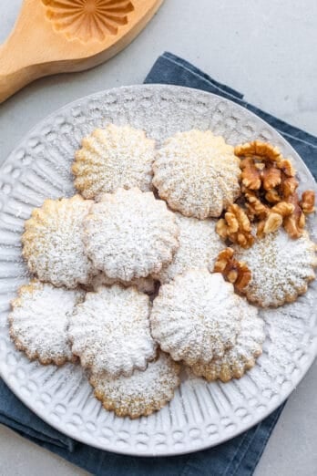 Maamoul cookies on a round decorative plate with extra walnuts dusted with powdered sugar.