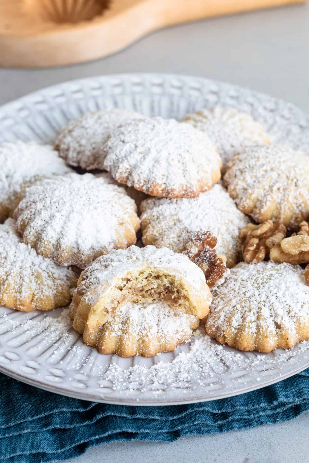 Walnut filled maamoul cookies on a plate dusted heavily with powdered sugar with cookie press nearby.