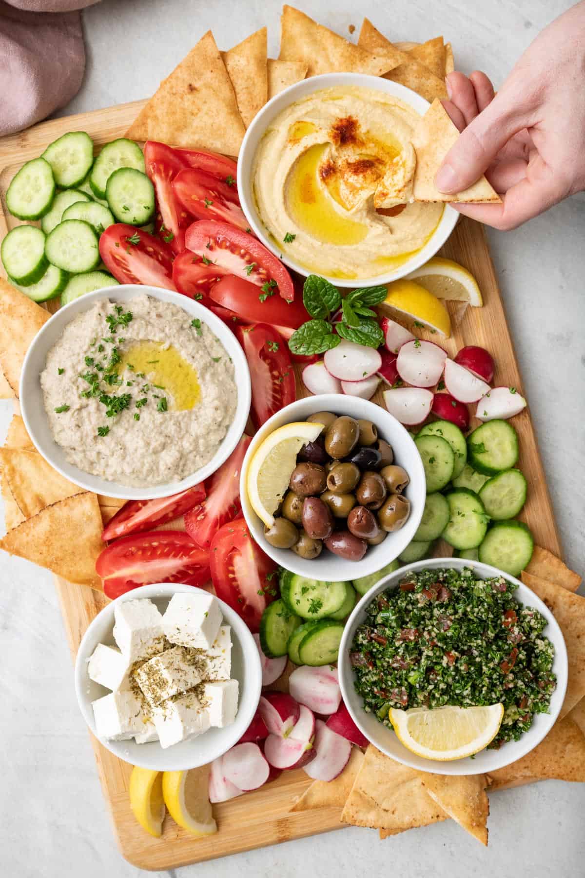 Hand dipping a pita chip into a bowl of hummus from a mezze platter spread with varies dips and vegetables.