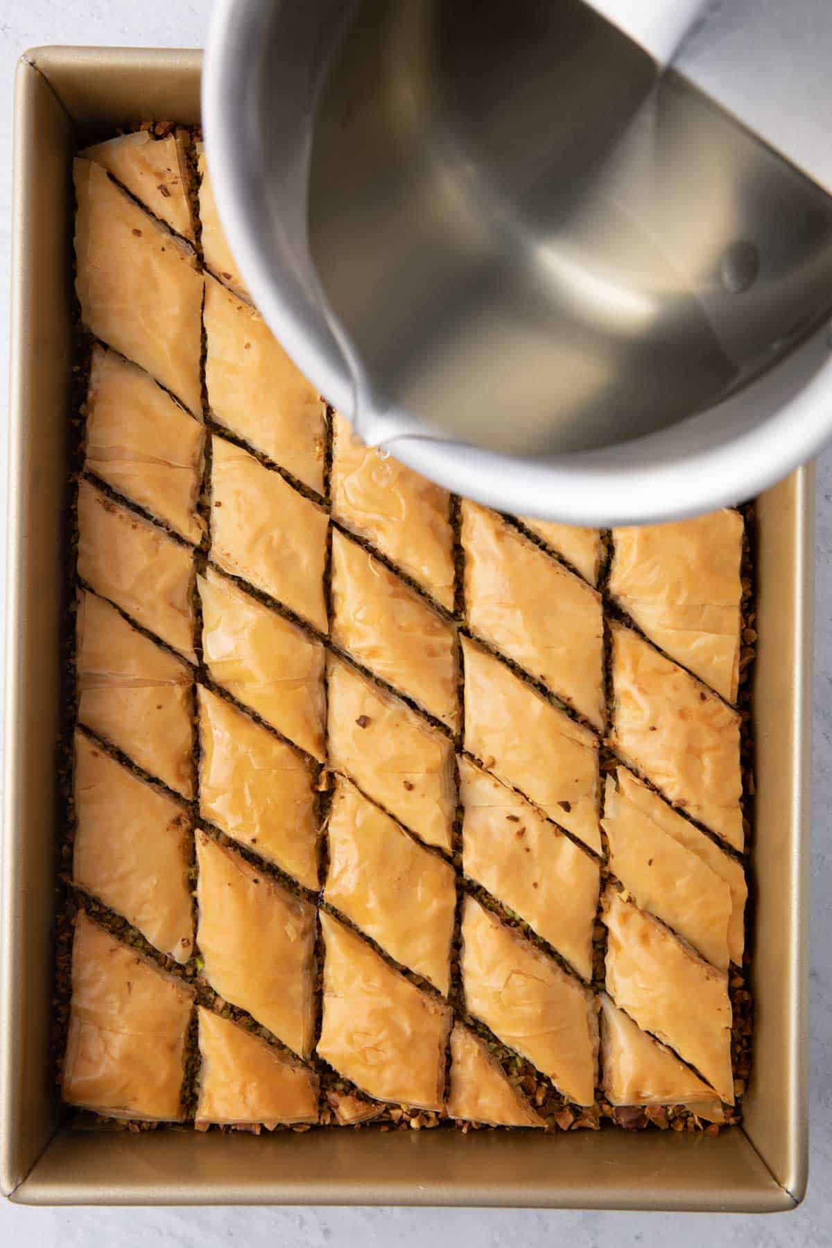 Simple syrup being poured over baklava from pot.