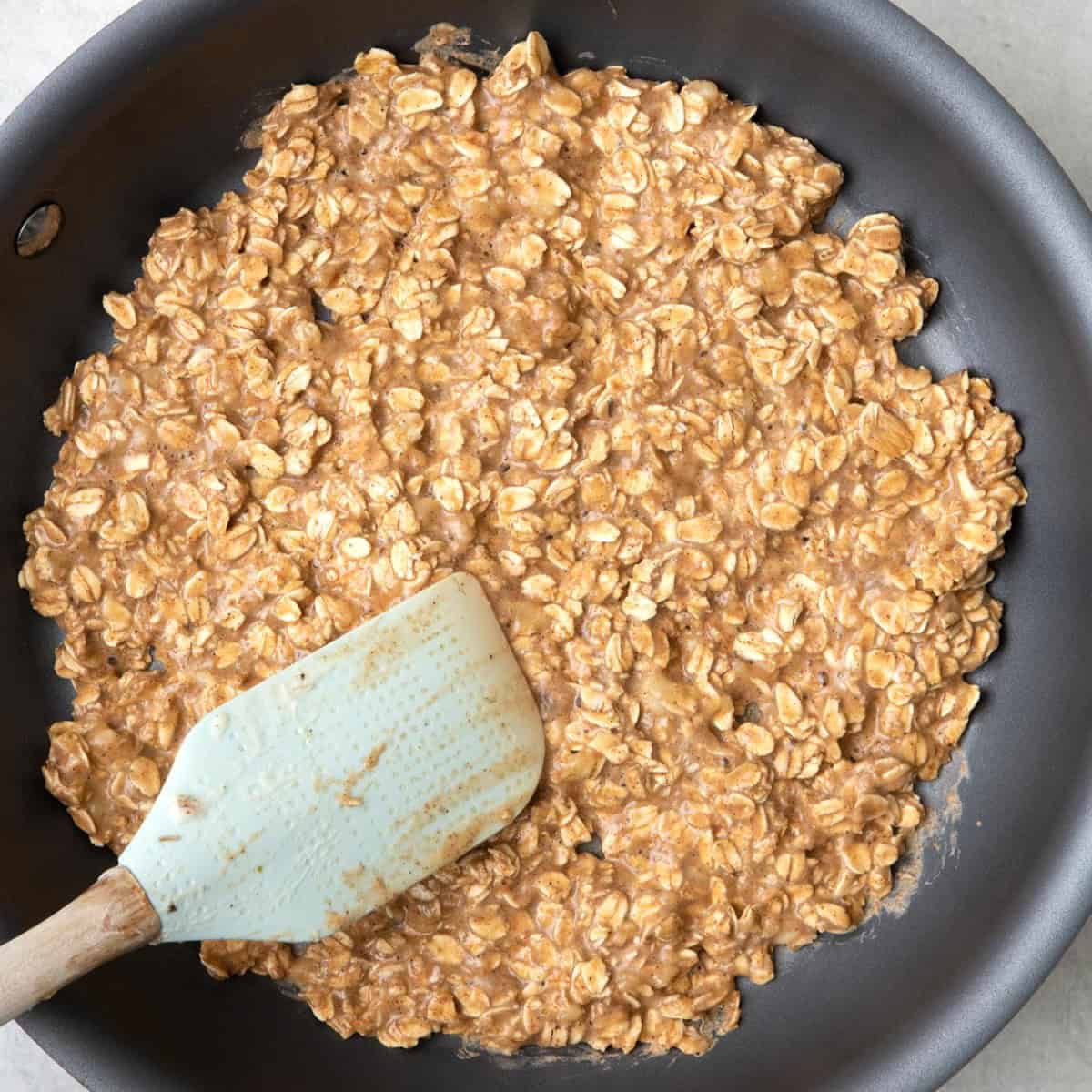 Oat mixture in a skillet with a spatula spreading it out.