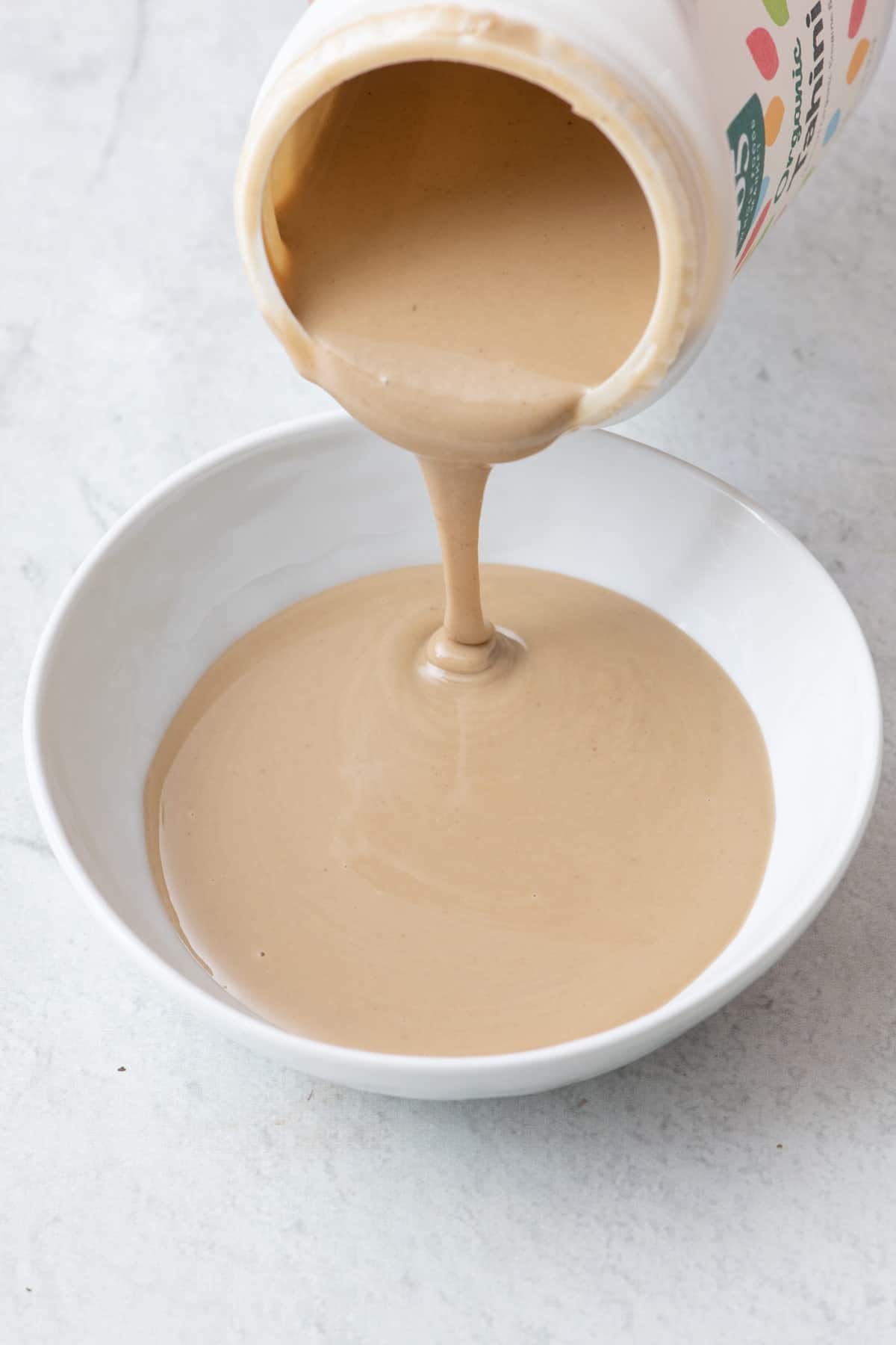 Tahini being poured into a bowl from a jar.
