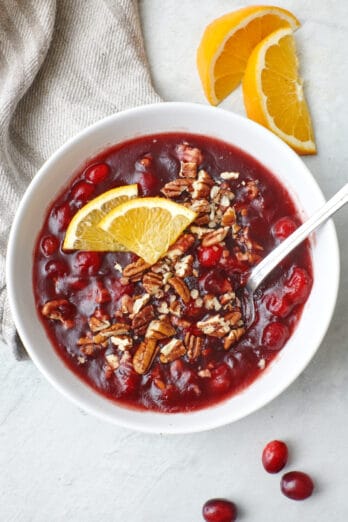 Baked Cranberry Relish in a white bowl and spoon, garnished with orange slices and pecans