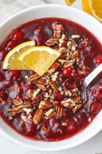 Baked Cranberry Relish in a white bowl and spoon, garnished with orange slices and pecans