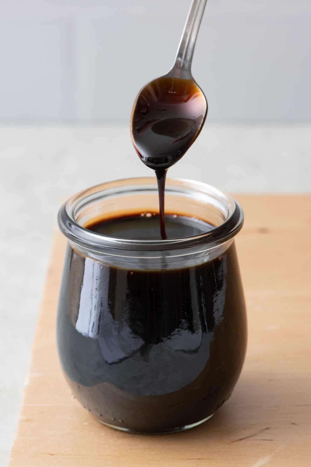 Balsamic glaze in a small glass jar with a spoon lifting some up and drizzling back into the jar.