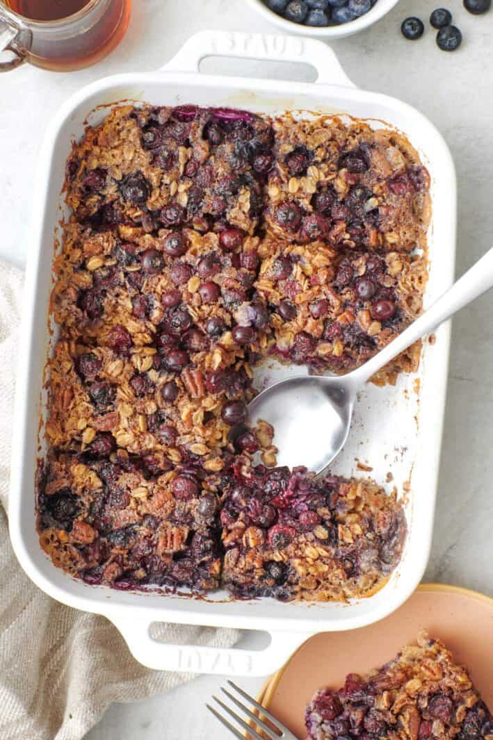 Baked blueberry oatmeal cut into 8 portions with a serving removed to a plate nearby.