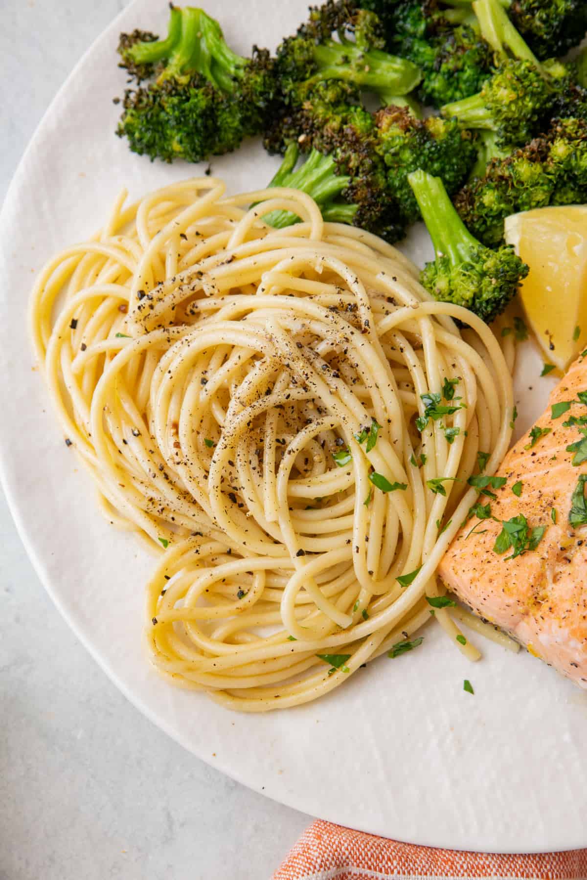 Cacio e Pepe on a plate with broccoli and salmon, garnished with fresh cracked pepper and chopped parsley.