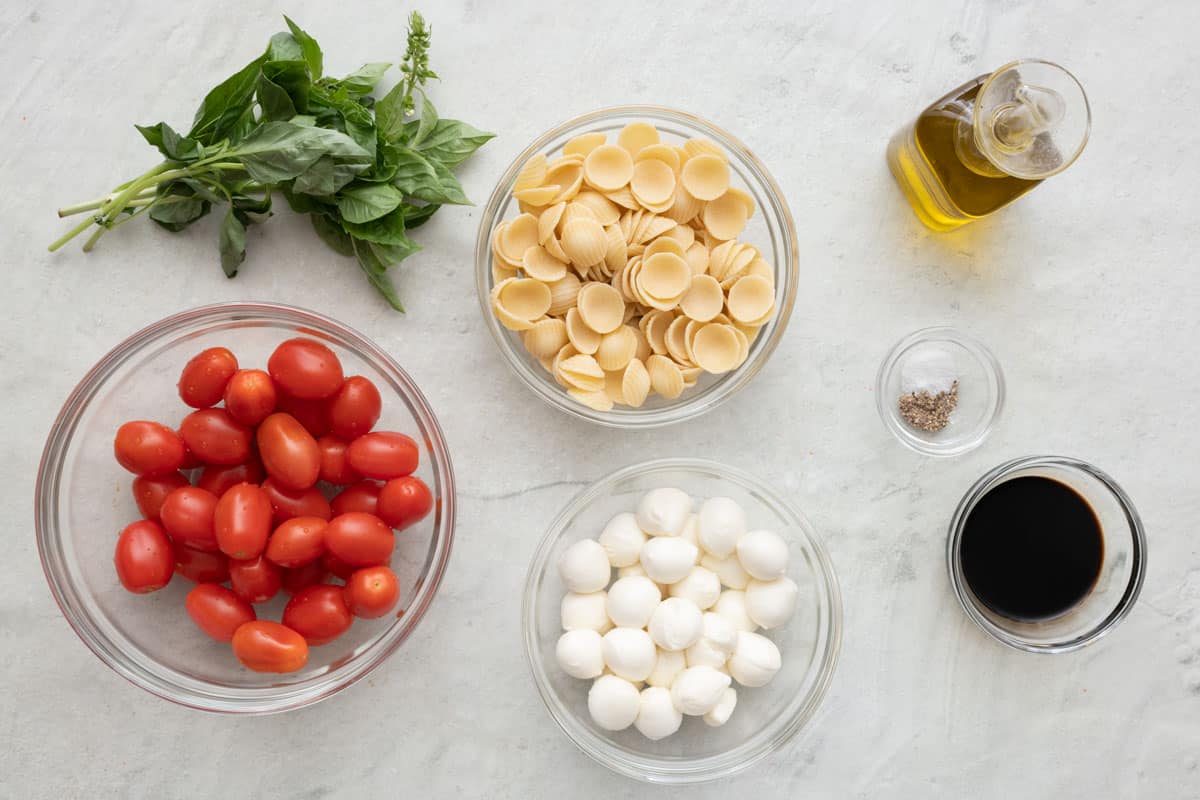 Ingredients for recipe before prepping: basil, tomatoes, pasta, mozzarella balls, oil, salt and pepper, and balsamic vinegar.