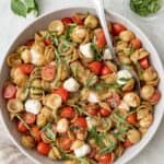 Caprese pasta salad in a large serving bowl with a spoon dipped in and extra sliced fresh basil sprinkled on top.