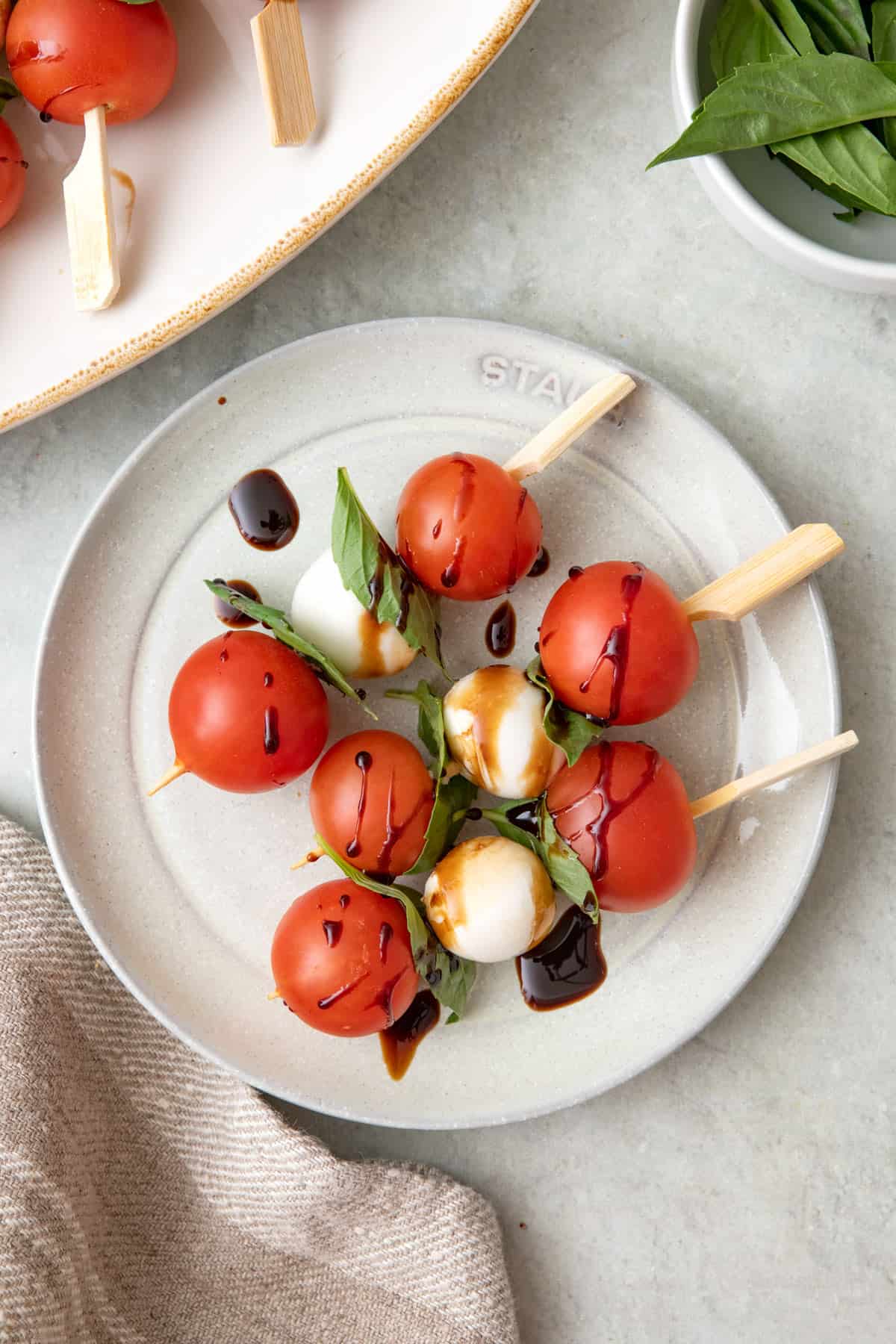 Three caprese skewers on a small plate with balsamic vinaigrette drizzled on top.