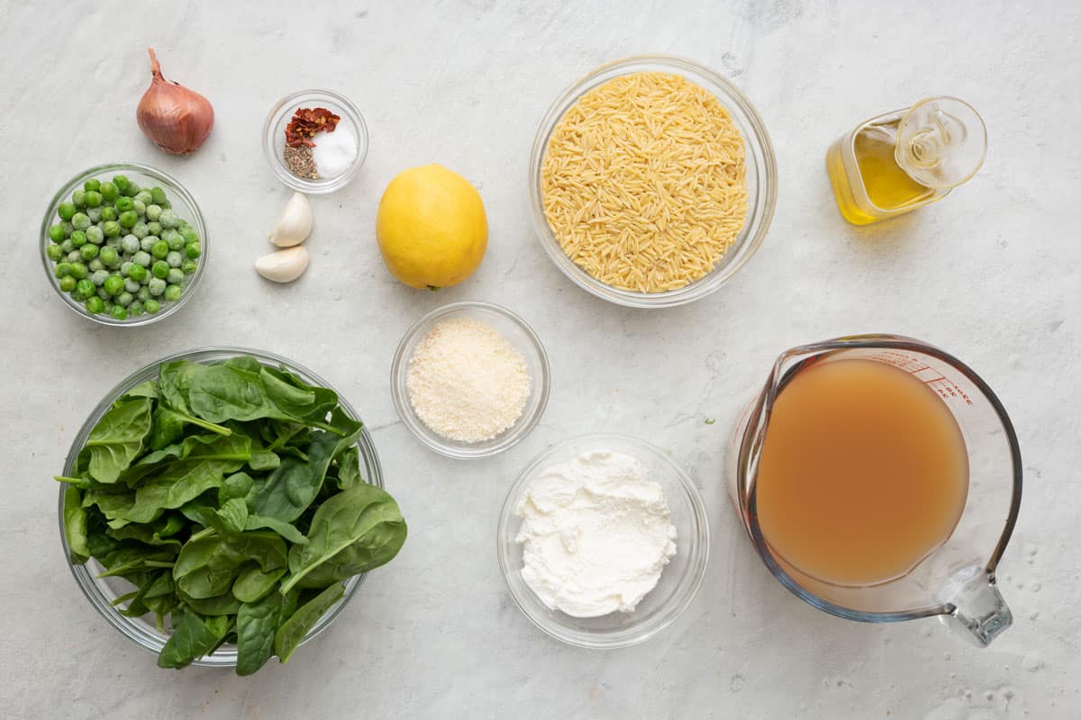 Ingredients for recipe before prepping: frozen peas, spinach, shallot, garlic, spices, lemon, parmesan, ricotta, orzo, oil, and borth.