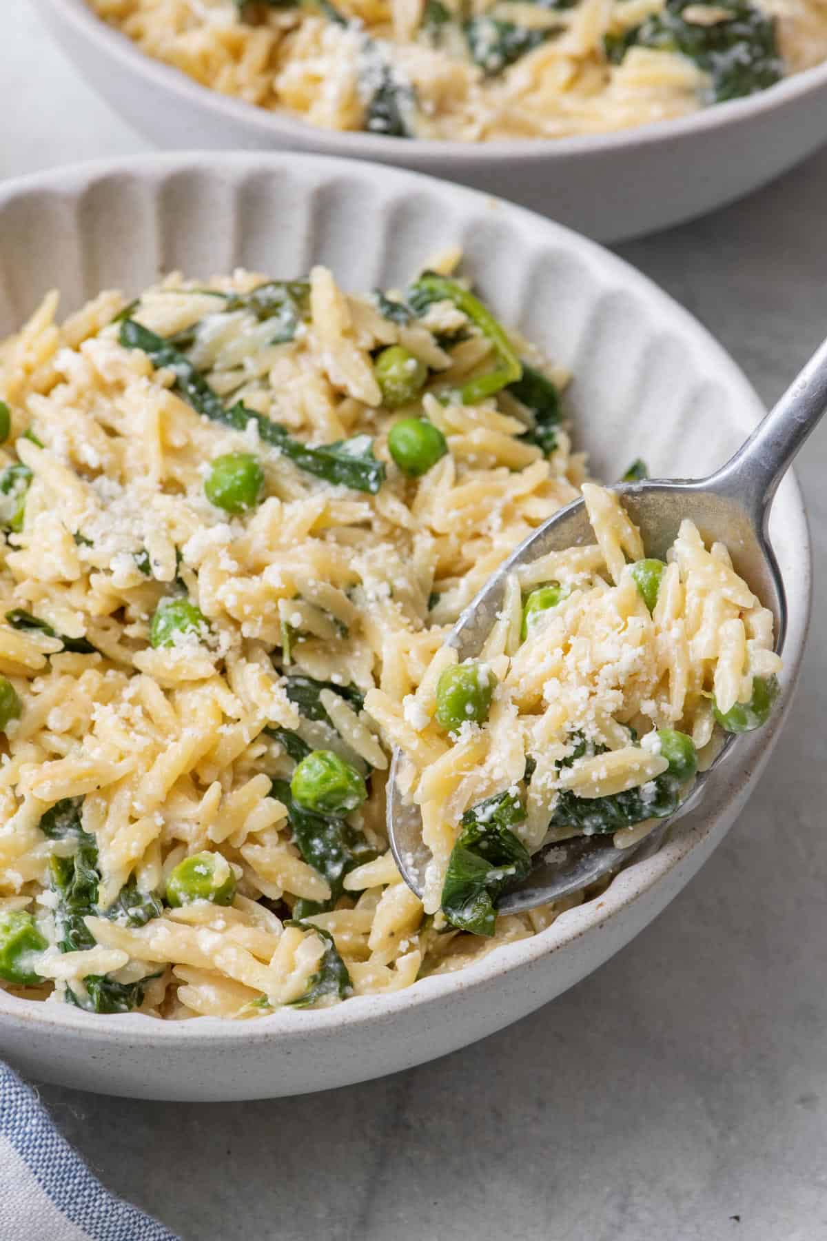 Spoon lifting up a bite of cheesy lemon orzo with peas.