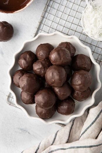 Chocolate coconut balls on a decorative plate with extra shredded coconut and melted chocolate nearby.
