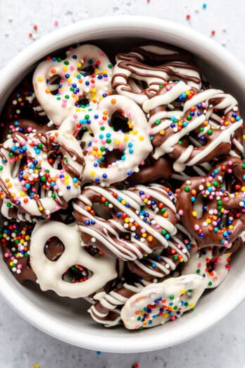 Chocolate-covered pretzels with rainbow sprinkles in a small bowl.