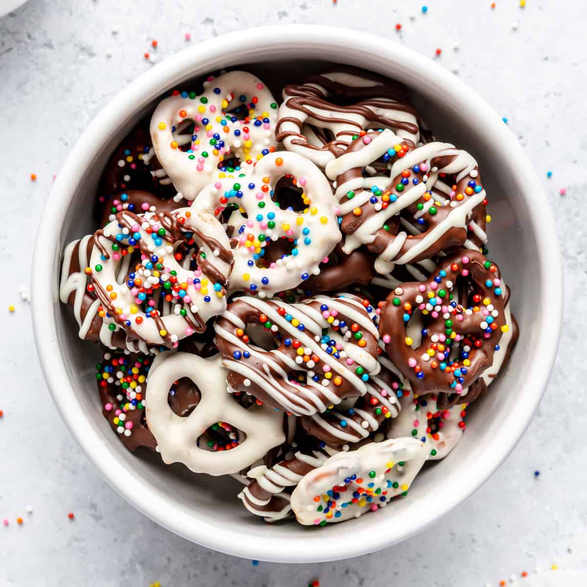 Chocolate-covered pretzels with rainbow sprinkles in a small bowl.