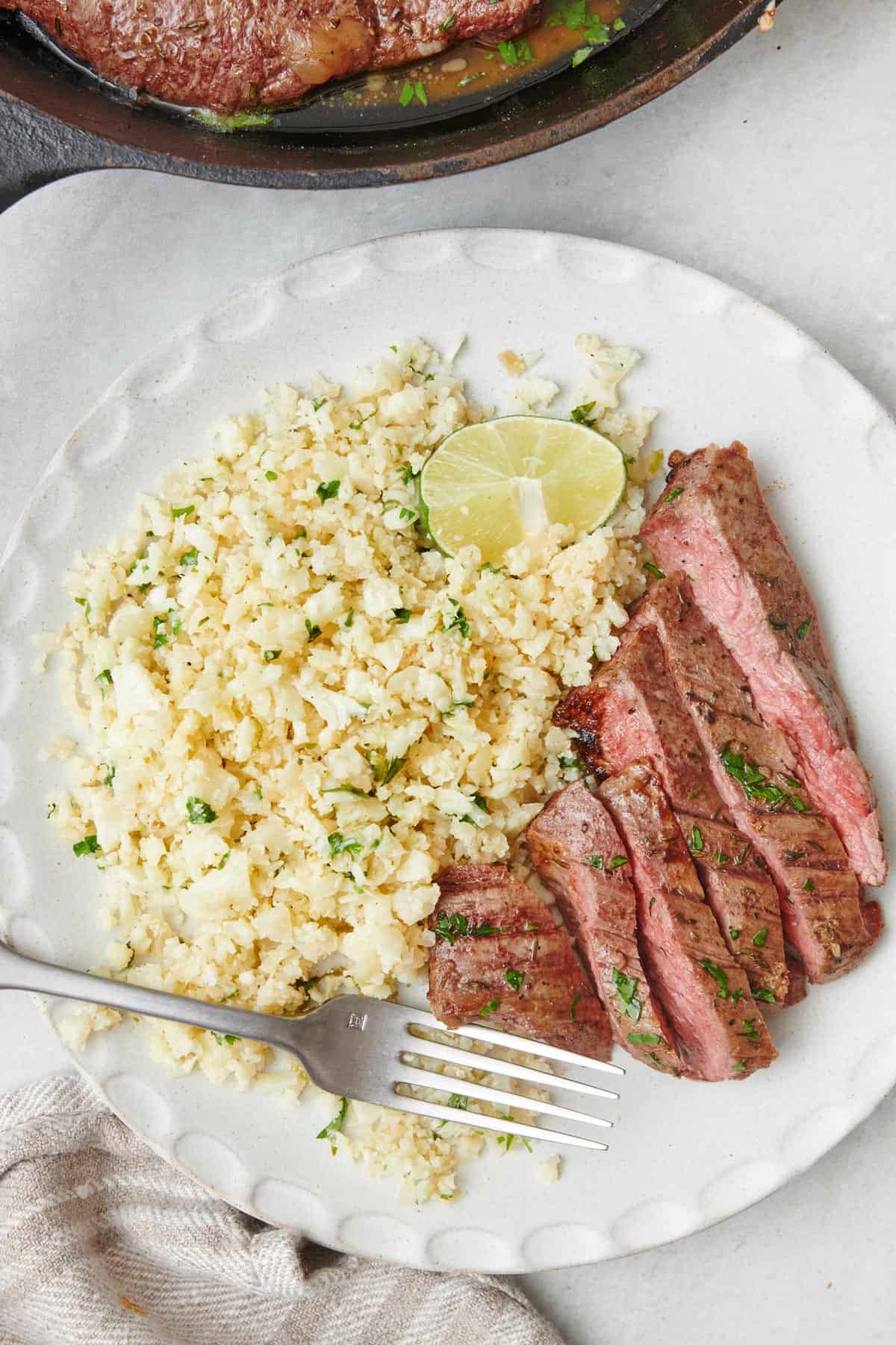 Plate of cilantro lime cauliflower rice with flank steak cooked medium rare.