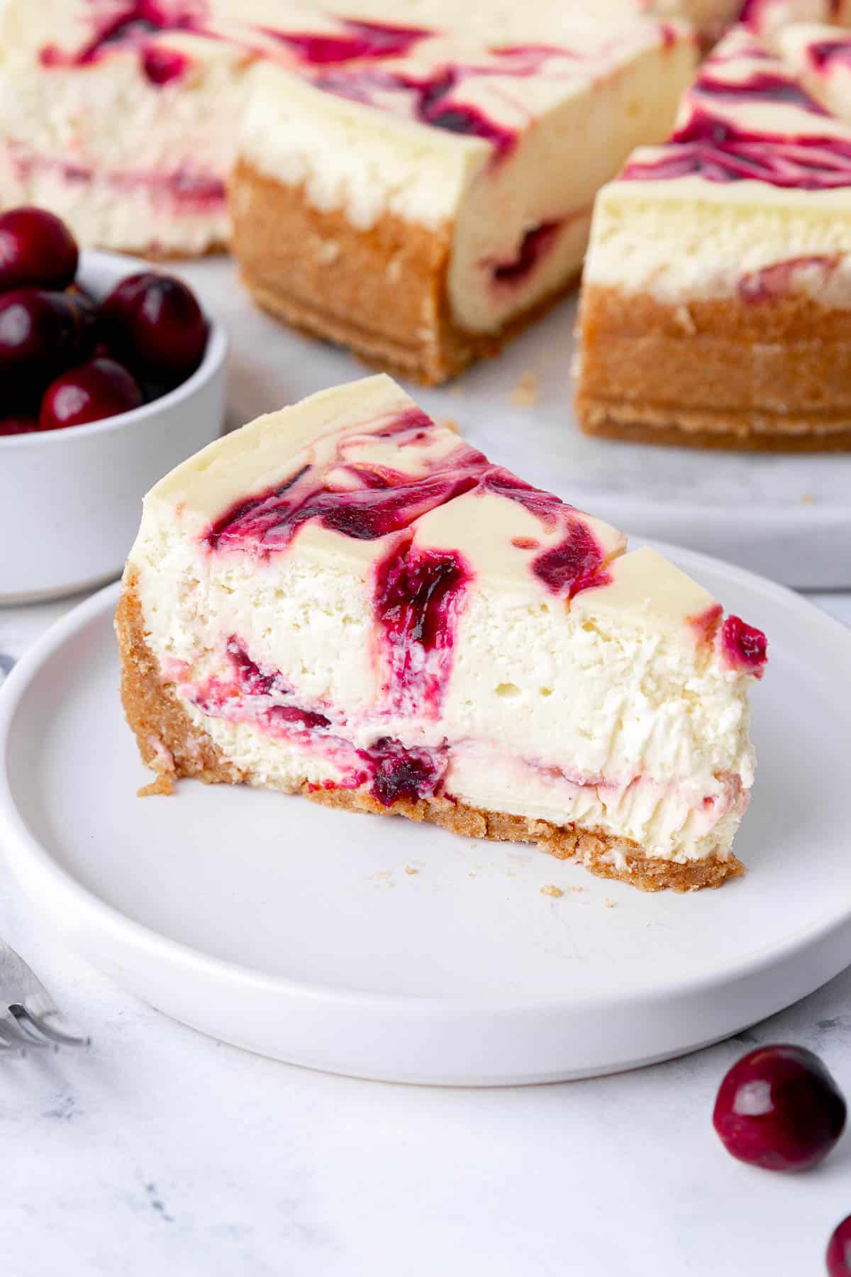 Slice of cranberry swirl cheesecake on a plate to show inside texture and layers of cranberry throughout.