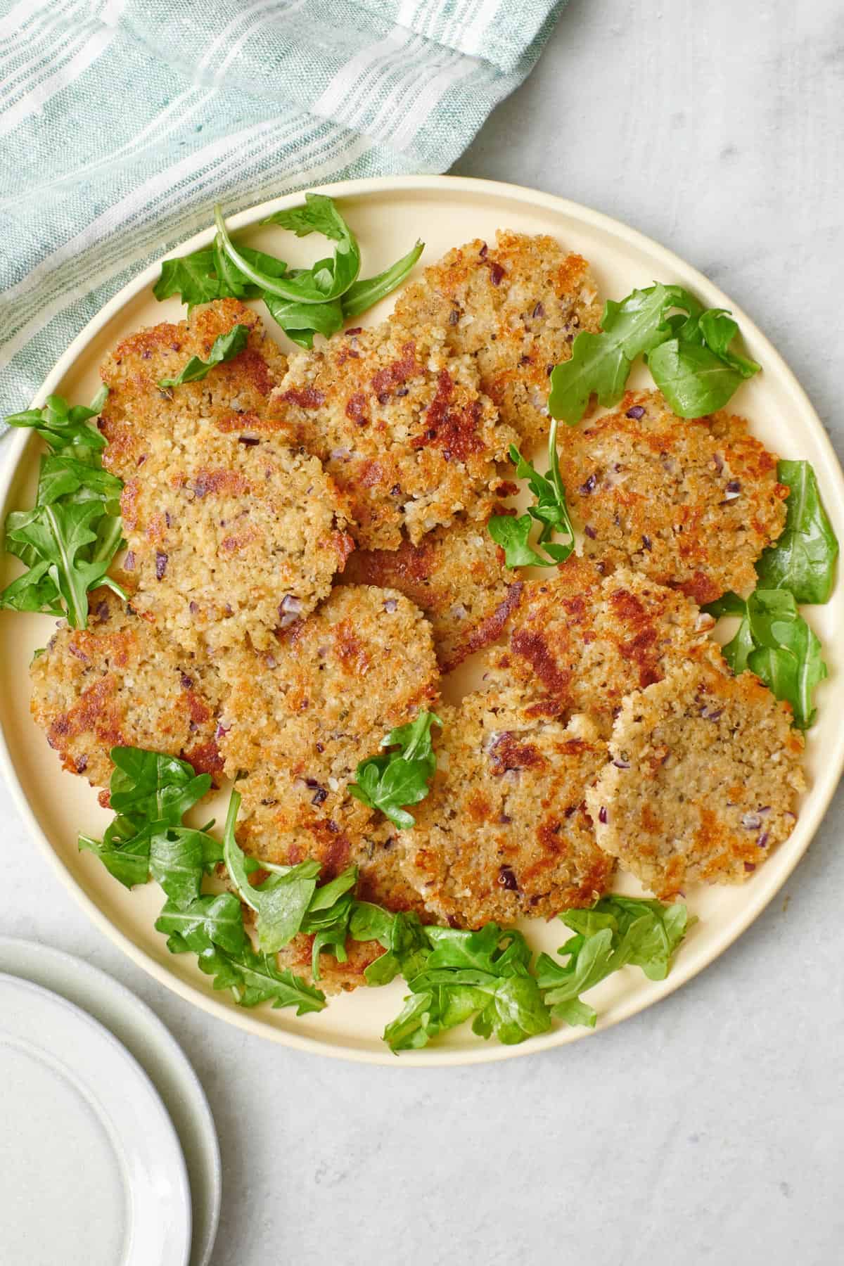 Crispy quinoa patties on a round plate with fresh greens.