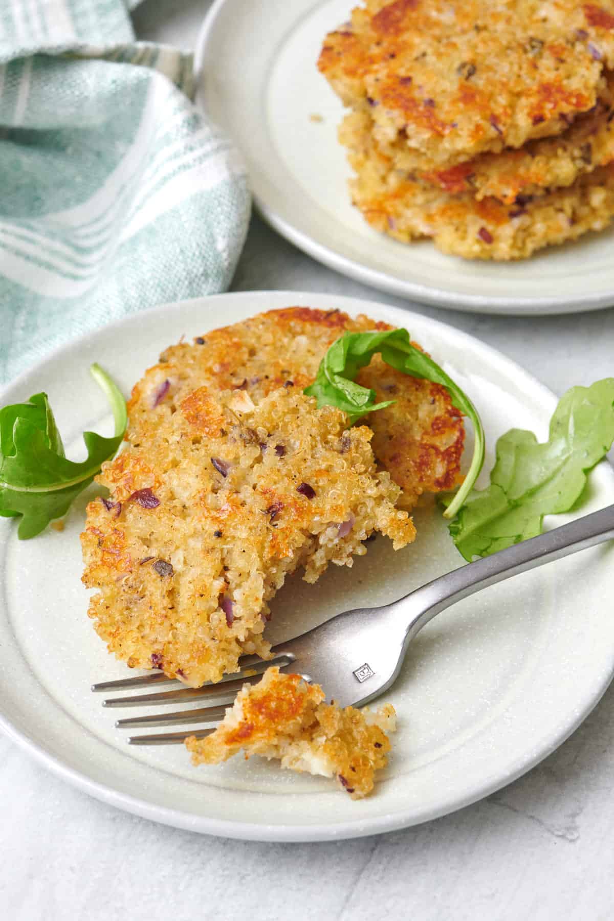 A few quinoa patties on a small plate with a fork and bite taken, small plate of more nearby.