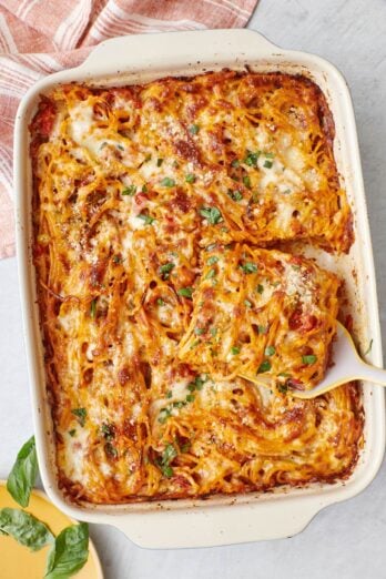 Baked spaghetti in a large baking dish with a serving being lifted out with a spatula.