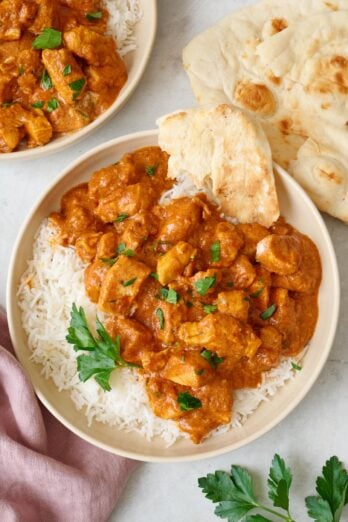 Easy Butter Chicken over rice in a bowl with a piece of torn flatbread on the side and another serving nearby.