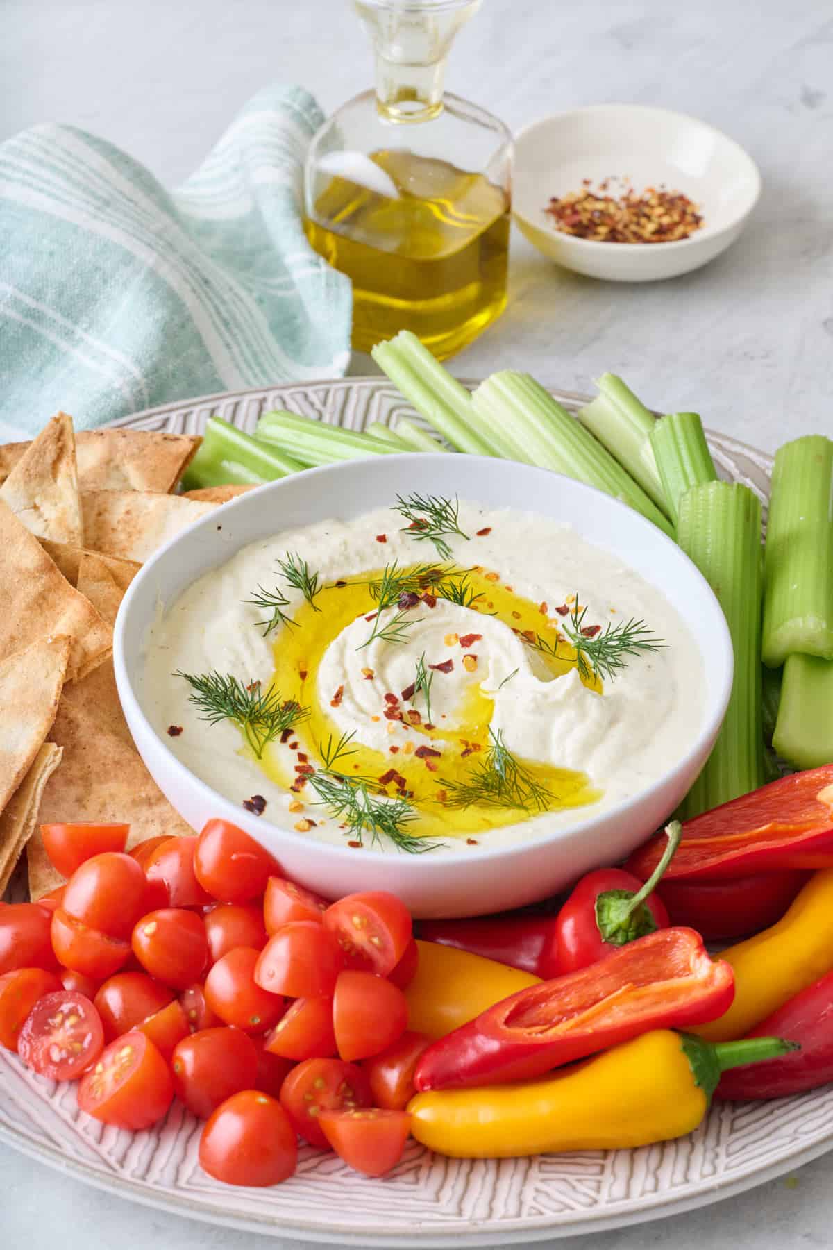 Creamy feta dip topped with oil and fresh dip on a platter with cherry tomatoes, peppers, celery sticks and pita chips.